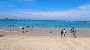 Ein Strand mit Menschen, die spazieren gehen und surfen, und einem strahlend blauen Himmel.