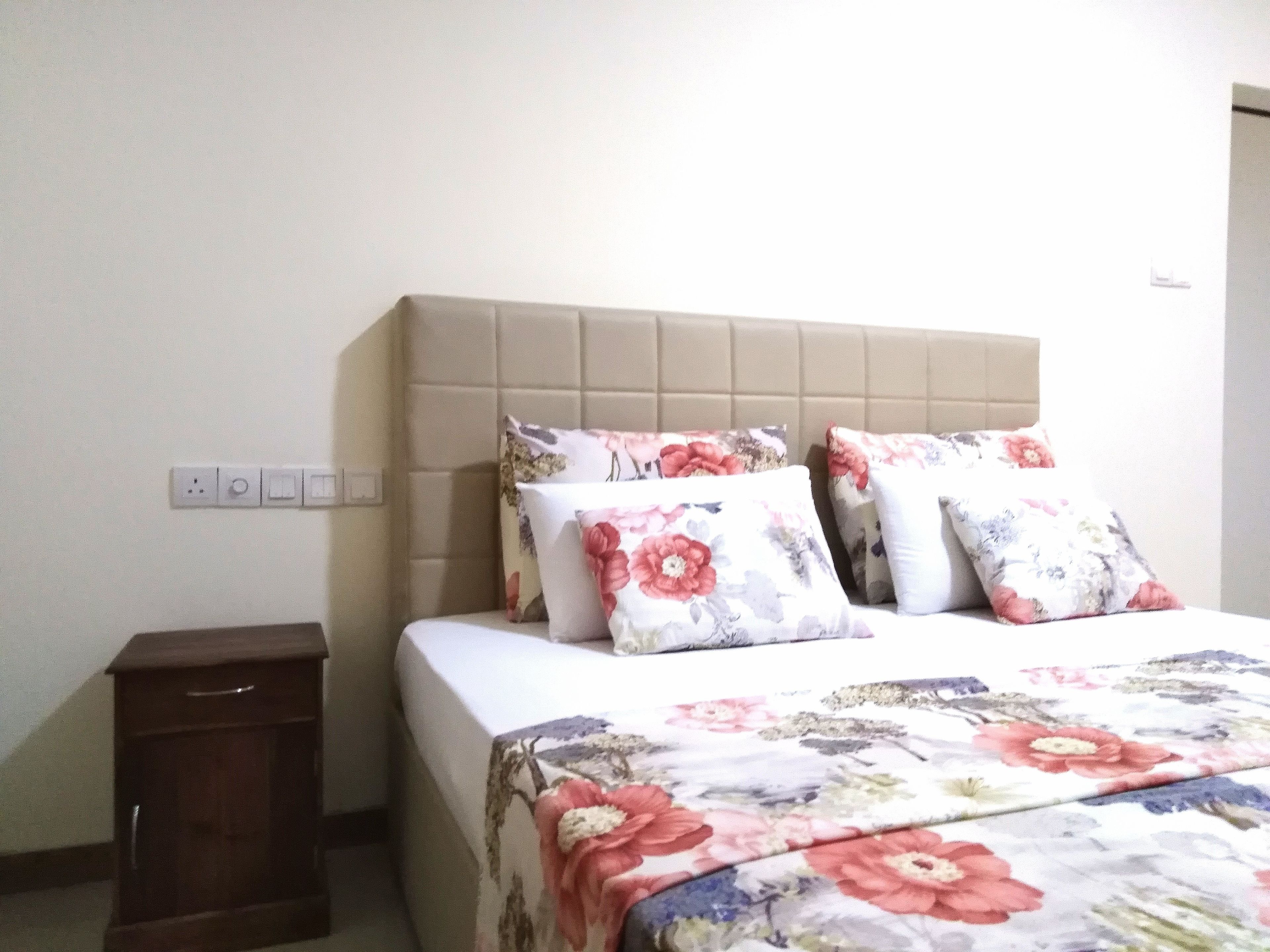 Une chambre à coucher avec un lit, deux oreillers, une table de chevet et une prise électrique au mur.