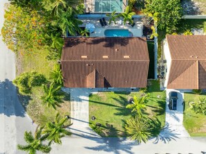 A residential property with a swimming pool, two houses with brown tiled roofs, and surrounding greenery.