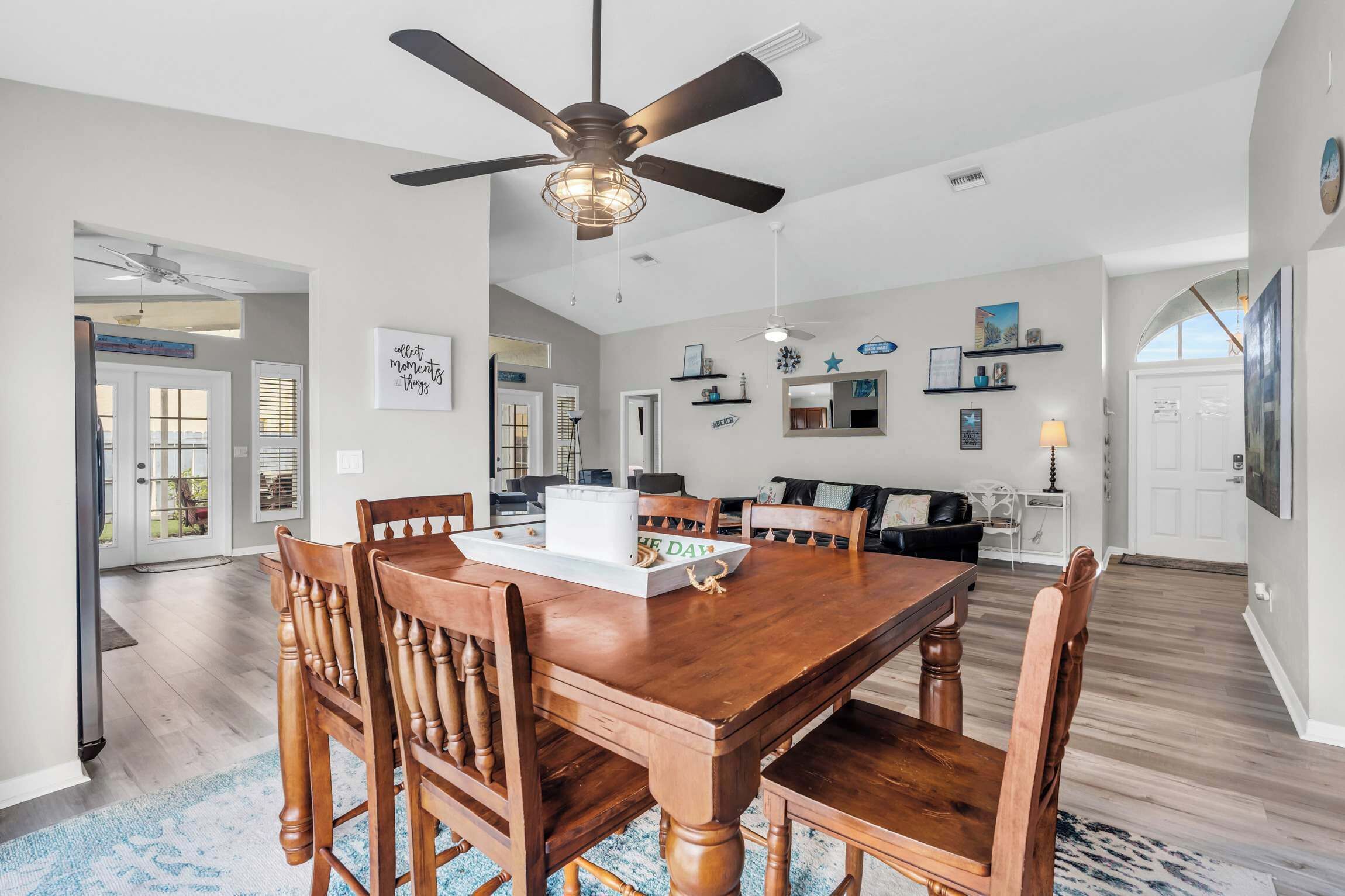Un vaste espace à manger avec une table et des chaises en bois, un ventilateur de plafond et une vue sur le salon attenant.