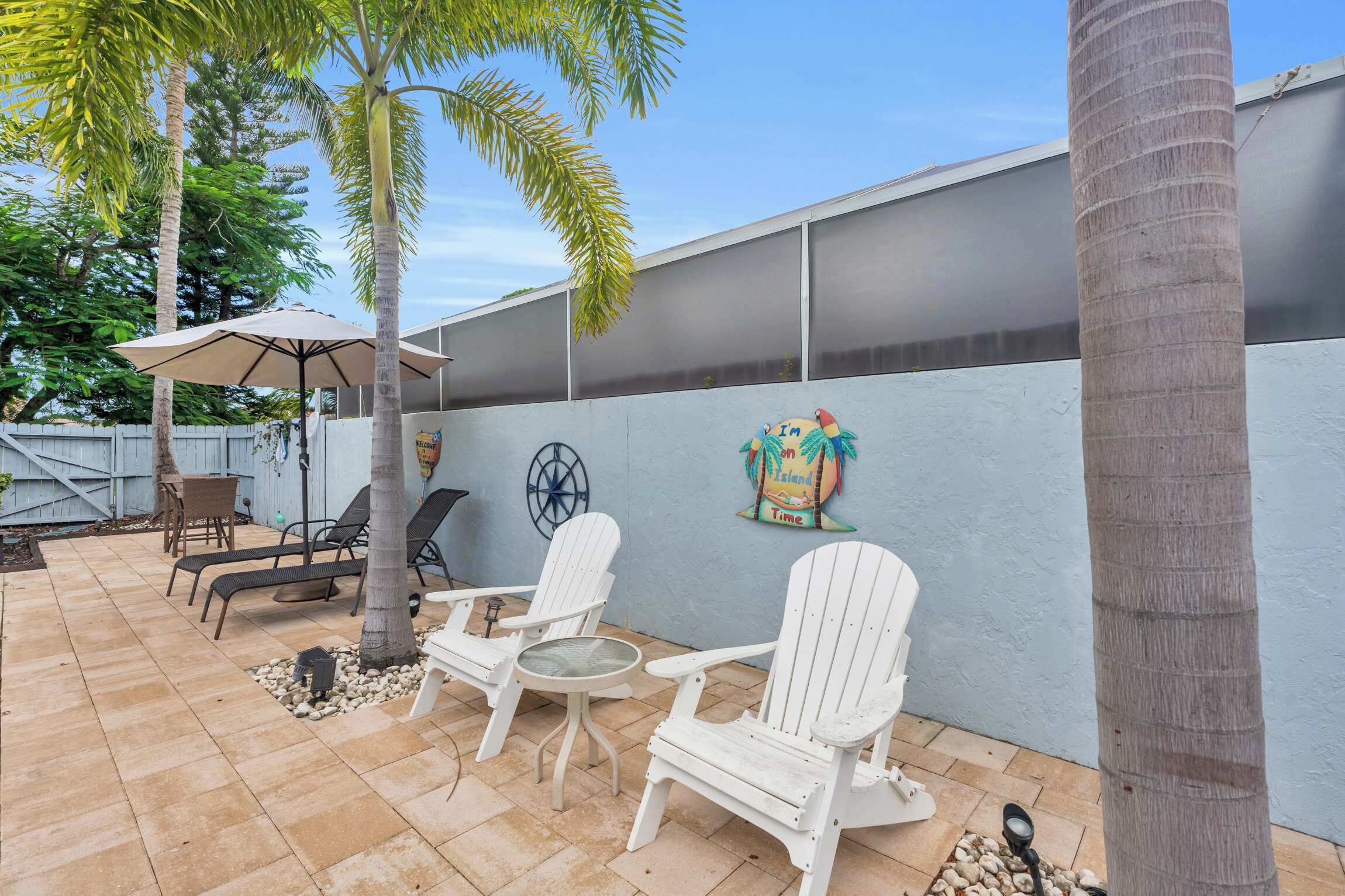 Une terrasse extérieure avec des chaises Adirondack blanches, une table et un parasol.