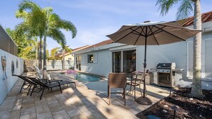 Un jardin avec une piscine, du mobilier de jardin, un barbecue et des palmiers.