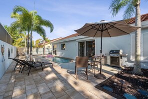 Ein Garten mit Swimmingpool, Terrassenmöbeln, Grill und Palmen.