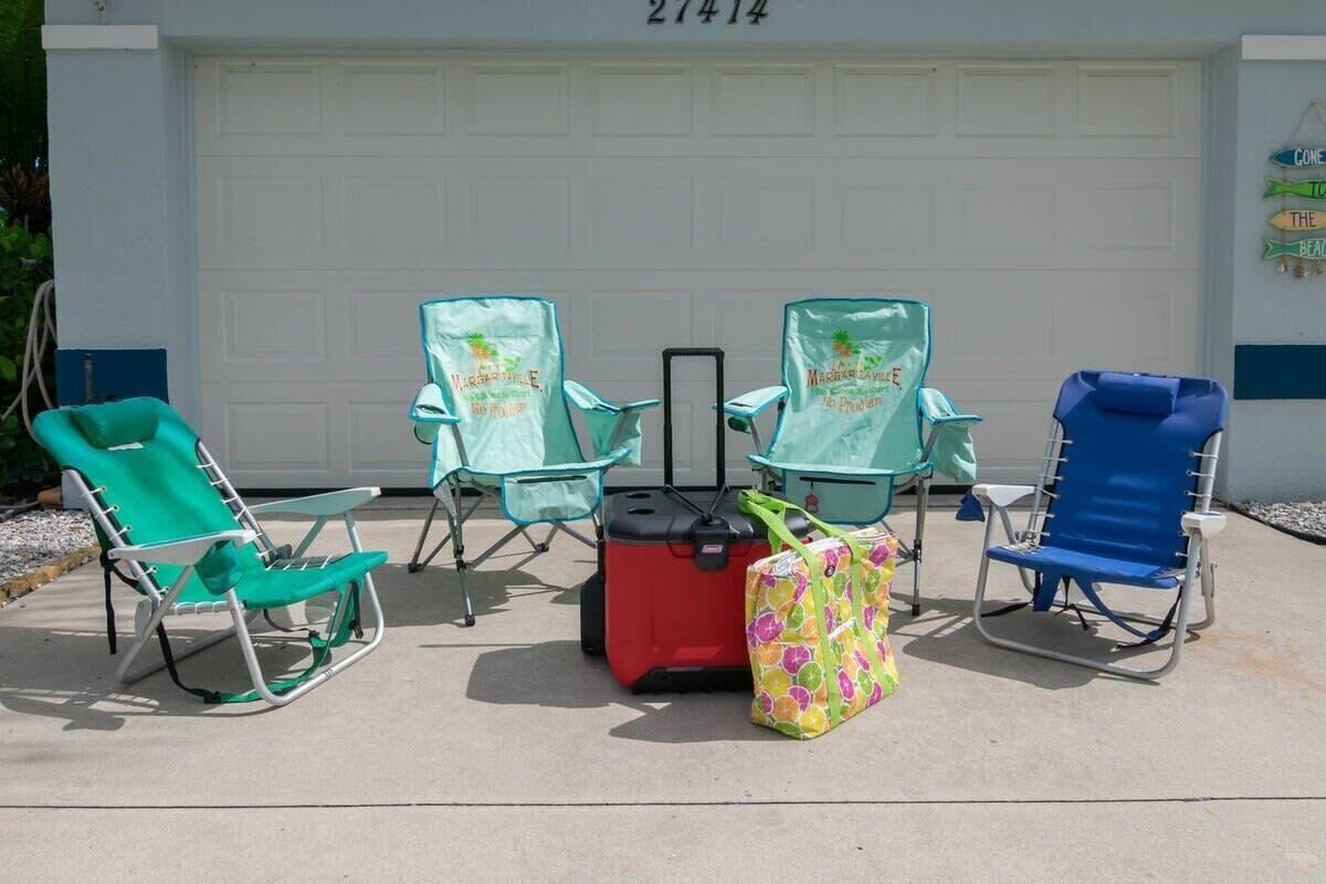 A garage with a white door, three beach chairs, a red suitcase, and a colorful bag.