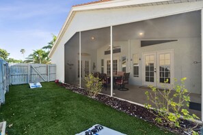 A covered patio area with a dining table and chairs, a small garden with a plant, and a fenced backyard.