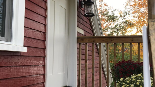 A wooden deck with a white door, a lantern, and a potted plant with red and yellow flowers. - The Nest ~ Quiet location close to shops, dining and Downtown Freeport. (Freeport)