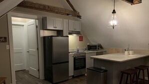 A compact kitchen with a refrigerator, microwave, oven, and a small island with stools. - The Nest ~ Quiet location close to shops, dining and Downtown Freeport. (Freeport)