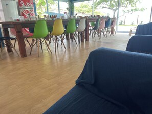 Un coin repas avec une longue table, des chaises colorées et un réfrigérateur en arrière-plan.