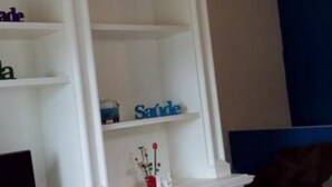 Una estantería blanca de varios niveles con un pequeño jarrón de flores en el estante superior.