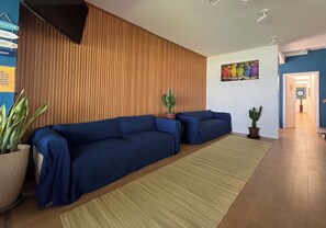 Une pièce avec un canapé bleu, un mur lambrissé en bois, une plante verte et un tableau représentant un oiseau aux couleurs vives.