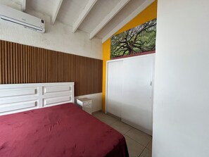 A bedroom with a bed, a wardrobe, a nightstand, and a wall-mounted air conditioner.