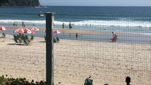 Una playa con un área delimitada por una red, sombrillas y gente.