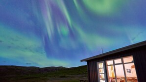 A building with a large window, a wooden deck, and a view of the night sky with the Northern Lights.