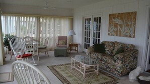 Ein Wohnzimmer mit weißen Möbeln, einem Glastisch und einem blumengemusterten Sofa.