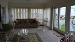 Ein Wohnzimmer mit einer Couch, Sesseln, einem Glastisch und Blick durch große Fenster.