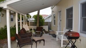 Eine überdachte Terrasse mit Korbmöbeln, einem Grill und einer weißen Bank.