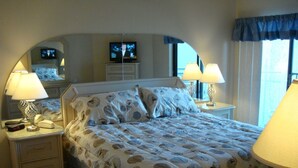 A hotel room with a large bed, two bedside tables, a television, and a window with curtains.