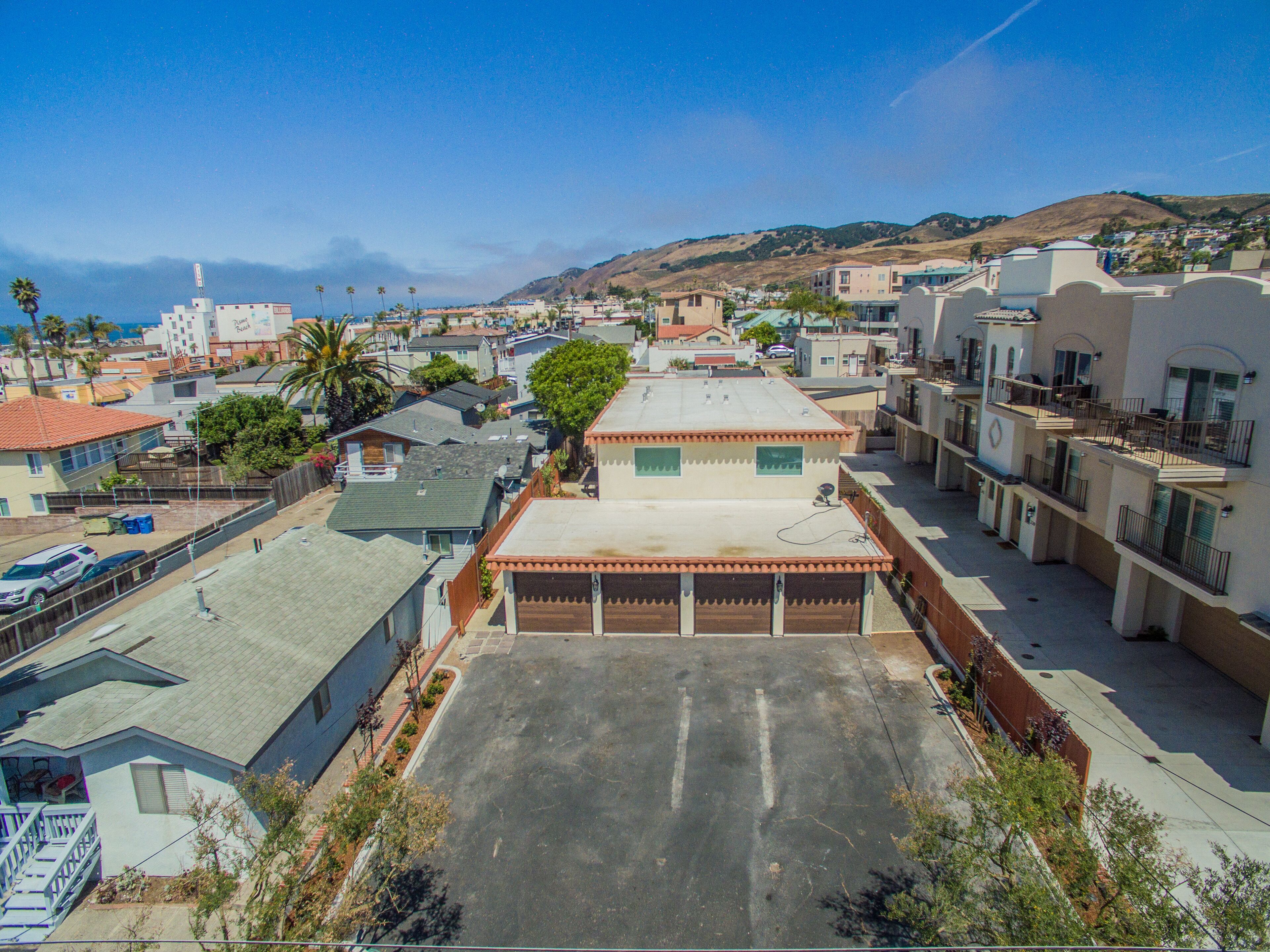 A residential area with a large open parking lot, multiple buildings with balconies, and a hilly landscape in the background.