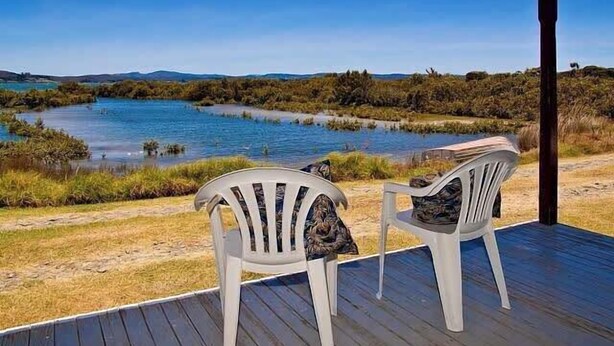 Una terraza con dos sillas blancas orientadas hacia el agua.