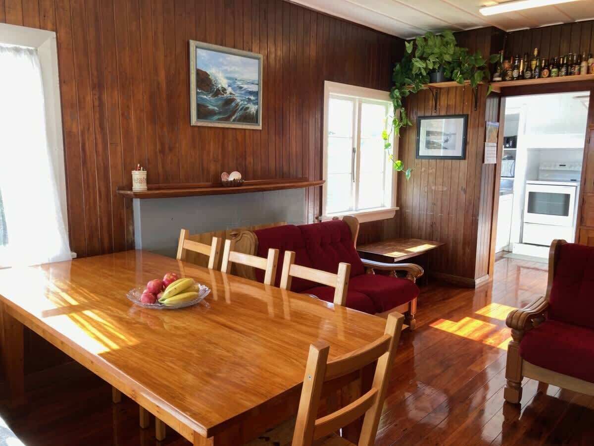 A wooden dining table with chairs, a red sofa, and a kitchen area with a refrigerator and shelves.