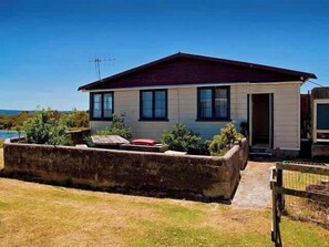 Una casa de un piso con techo rojo, un plato de satélite visible, y un jardín delantero con un parterre elevado.