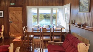 Un interior de madera con comedor, un sofá rojo y vistas a un lago a través de amplios ventanales.
