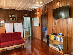 Ein Zimmer mit Holzwänden, einem roten Sofa, einem Fernseher und einem Bücherregal.