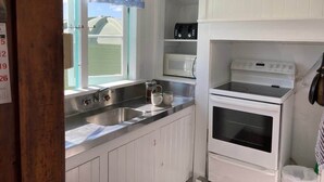 Una cocina con armarios blancos, un lavamanos de acero inoxidable, un microondas y un horno.