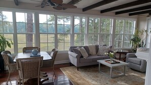 Un salon spacieux doté d’une grande fenêtre, d’un ventilateur de plafond et d’un coin repas avec des meubles en osier.