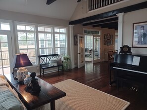 A spacious living room with a piano, a bench, and a large window overlooking a deck. - Peace on the Brewers River with Panoramic Views. (Carrollton)