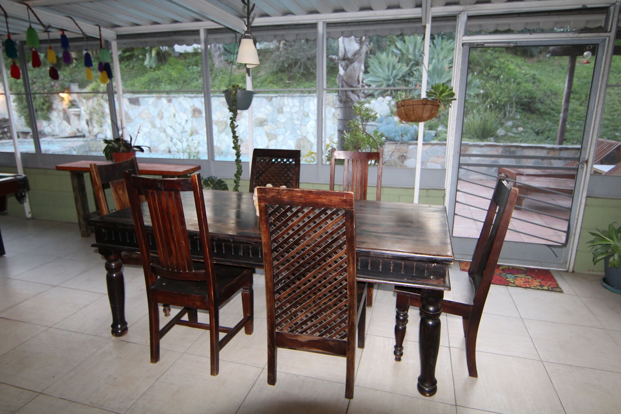 Un espace repas comprenant une grande table et des chaises, un luminaire suspendu et une vue sur la verdure à l’extérieur.