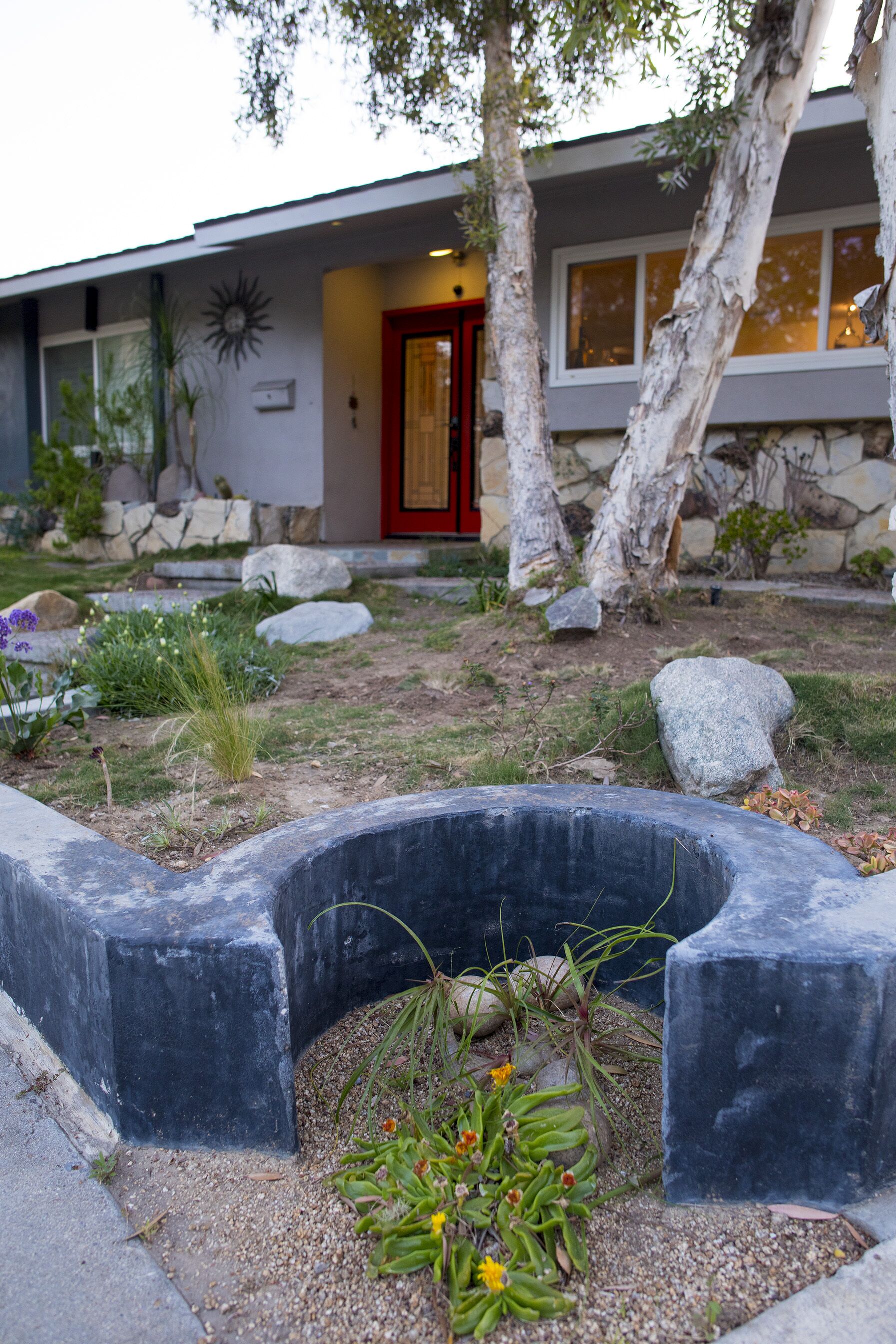 Et moderne hus med rødlakeret dør, stenvægge og en have med sten og beplantning.