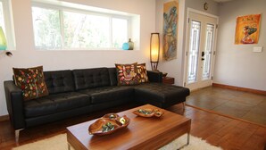 A living room with a dark leather sofa, decorative pillows, a wooden coffee table with glass marbles, a fluffy rug, and a painting on the wall.