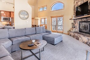A spacious living room with a grey sectional sofa, a round coffee table, and a stone fireplace.