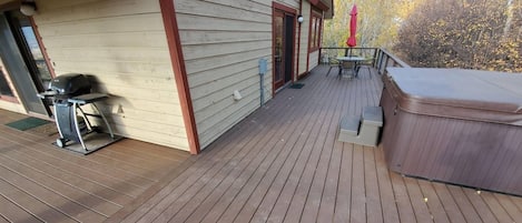 A wooden deck with a hot tub, outdoor seating, and a view of trees.