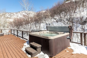 Un jacuzzi en una terraza de madera con vistas a colinas nevadas.