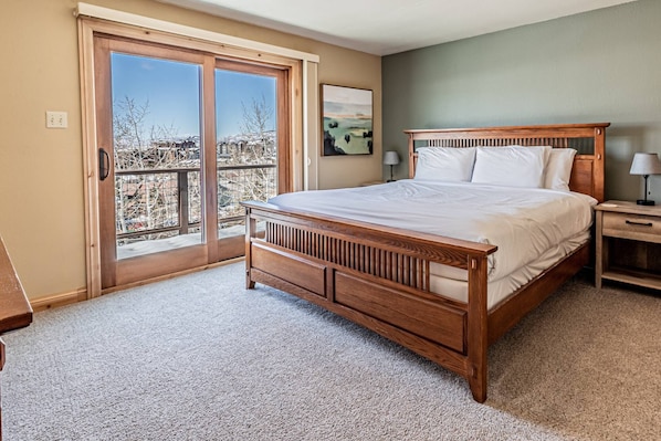 A bedroom with a wooden bed, a nightstand, a lamp, and a large sliding glass door leading to a balcony.