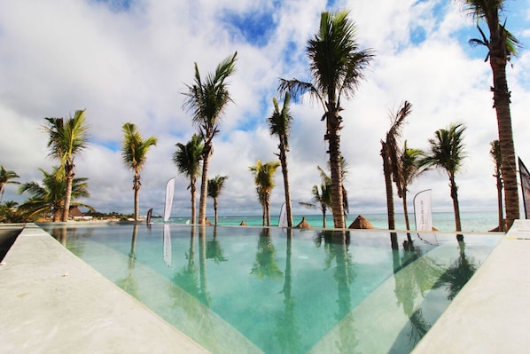 A clear pool with palm trees and a view of the ocean.