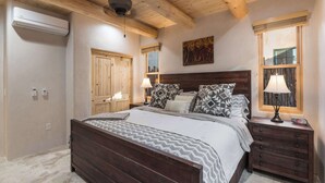 Un dormitorio con techo de madera, una cama con ropa de cama estampada, una mesita de noche con lámpara y un aire acondicionado instalado en la pared.