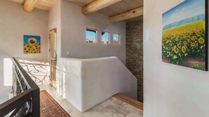 Un interior moderno con techo de madera, una pared blanca con una pintura de girasoles y una escalera con un tapete estampado.