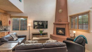 Un salón amplio con chimenea, sofás de cuero, un televisor de pantalla plana y un ventanal grande.