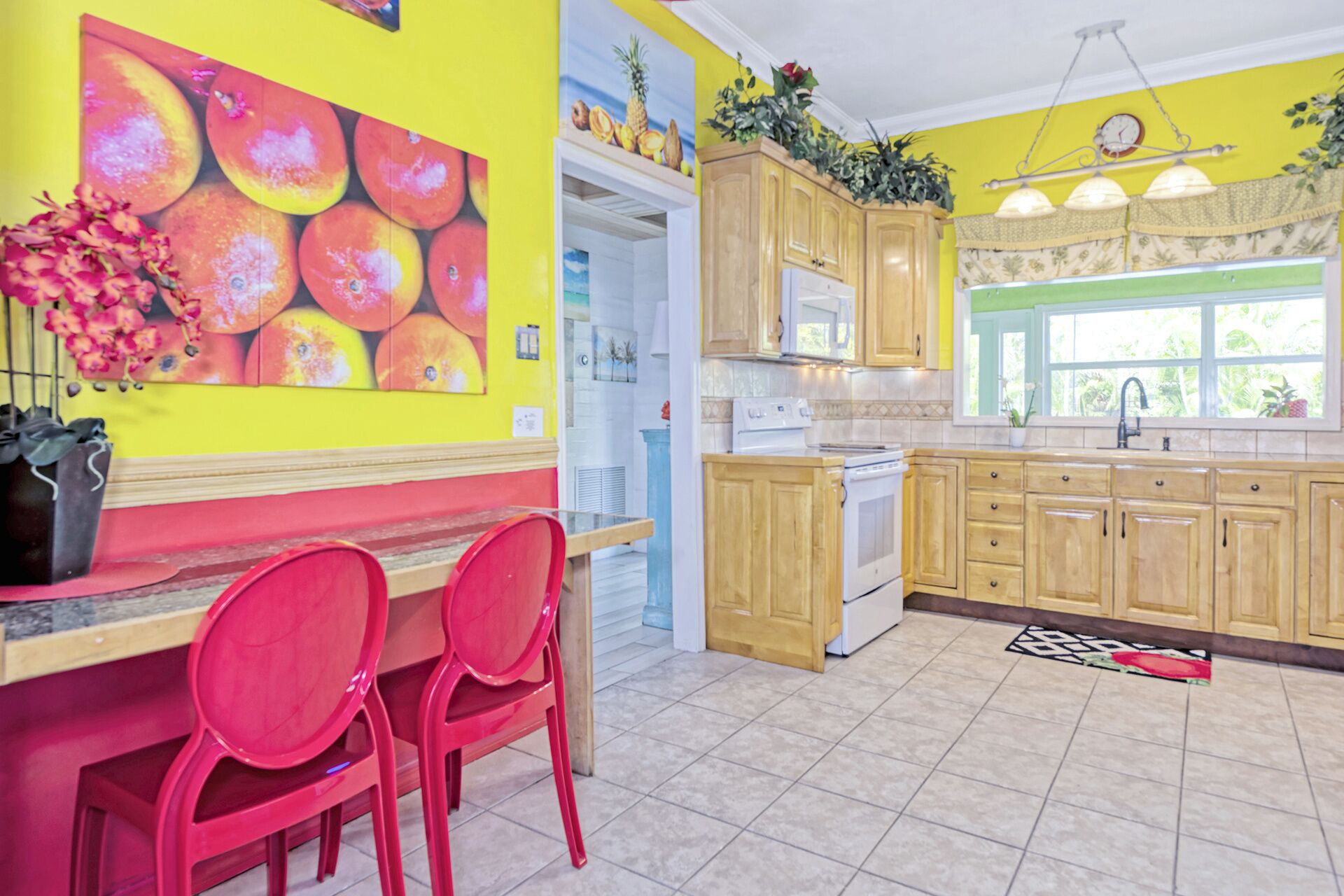 Una cocina con armarios de madera, una estufa blanca y una pared amarilla con una pintura de frutas.