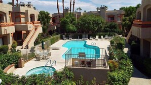 Zona de piscina con sillas de descanso y palmeras, rodeada de edificios con balcones y escaleras.