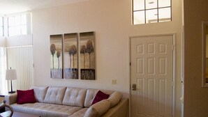 Un salón con un sofá seccional color beige, una mesita y una puerta. Hay tres obras de arte enmarcadas en la pared.