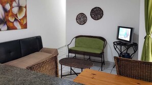 En stue med sofa, grøn polstret lænestol, lille bord og fjernsyn på et stativ.