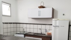 Et kompakt køkken med gasblus, hvide skabe, et køleskab og et lille spiseområde med en stol.