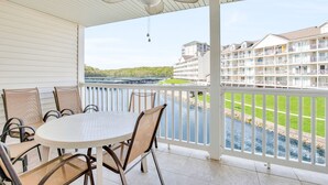 Un balcón techado con una mesa y sillas, con vistas a un río y un conjunto de edificios.