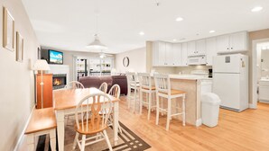 Una cocina moderna con armarios blancos, un microondas y un refrigerador. Hay un comedor con una mesa y sillas de madera.