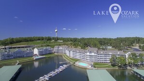 Un hotel frente al lago con varias edificaciones, un muelle con barcos y una torre al fondo.