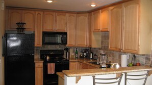 Una cocina con armarios de madera, un refrigerador negro, un microondas, un horno y una pequeña isla con dos taburetes de bar.